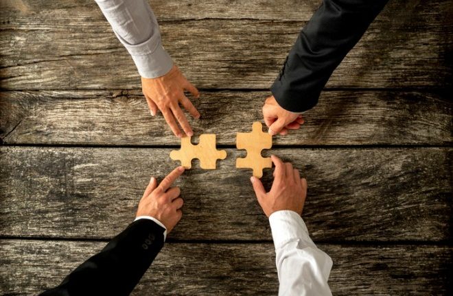 four hands with two puzzle pieces